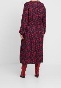 Vestido de manga larga en color azul marino con estampado floral rojo, cintura elástica y corte relajado. Combinado con botas rojas hasta la rodilla y un sencillo cuello redondo.