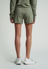 Olivově zelené šortky vyrobené z měkké bavlny, s jednoduchým, pohodlným designem a rovný lem, spárované s bílými atletickými botami.