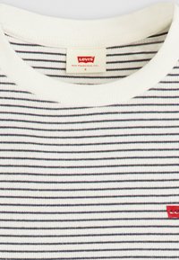 Bijela i tamnoplava prugasta majica s rebrastom teksturom. Ima okrugli izrez i mali crveni Levi's logo na prsima.