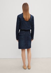 Vestido vaquero en azul oscuro con forma ajustada, mangas largas y dos bolsillos traseros. Textura suave, detalles de botones y dobladillo a la altura de la rodilla.