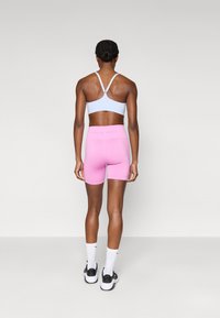 Αθλητικό σουτιέν ανοιχτού γαλάζιου με ρυθμιζόμενους ιμάντες· ροζ σορτς Nike Pro· λευκές κάλτσες αστραγάλου· αθλητικά παπούτσια σε μαύρο και άσπρο· ομαλή υφή ύφασματος.