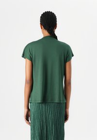 Maglietta verde a maniche corte con vestibilità morbida, texture liscia e orlo arrotondato, abbinata a una gonna verde plissettata che mostra un design a strati.
