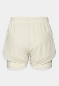 Pantalones cortos deportivos color crema con un panel lateral de malla. Tienen una cinturilla elástica suave y pantalones cortos ajustados interiores. Acentos de tela texturizada.