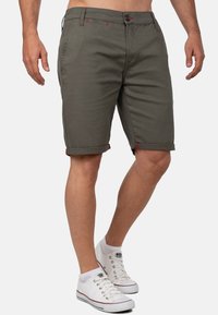 Grijze katoenen shorts met opgerolde manchetten, rode stiksels, voorzakken en een getailleerd ontwerp, gecombineerd met witte sneakers.