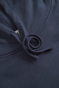 Primo piano del tessuto di una felpa con cappuccio blu navy che mostra l'area del cappuccio con i cordini legati e un'etichetta interna parzialmente visibile.
