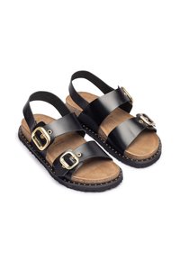 Sandalias de cuero negro con correas ajustables, herrajes dorados, plantilla de corcho y suelas de caucho con pequeños studs en los bordes.