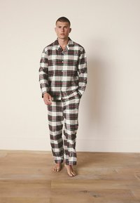 Set de pijama din flanel cu carouri în alb, roșu și negru. Include o cămașă cu butoni, cu guler, și pantaloni cu talie elastică asortate.