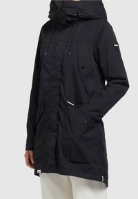 Svart parka-jacka med huva, dragkedja och tryckknappslås, justerbara dragsnören, flera framfickor och en texturerad tygfinish.