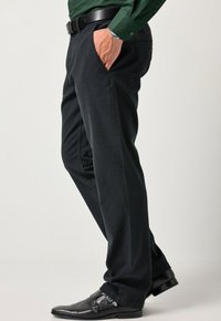 Pantaloni grigi scuri con una texture liscia e tasche laterali, abbinati a scarpe in pelle nera con doppia fibbia. Includi una cintura in evidenza.