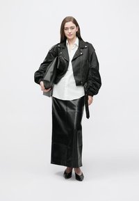 Black leather bomber jacket with puffed sleeves, white button-up shirt, black leather midi skirt, and black heels, holding a clutch bag.