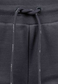 Dunkelgraue Jogginghosen verfügen über einen gerippten Bund mit Kordelzug, kontrastierenden Nähten und einer glatten Textur.