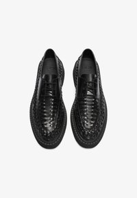 Chaussures noires en cuir avec un motif tissé, présentant un bout lisse, un système de laçage et une semelle noire robuste. Accents texturés sur l'ensemble.