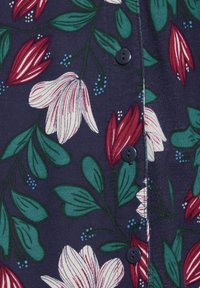 Marine stof met grote witte en rode bloemen en groene bladeren. Zwarte knopen accentueren het ontwerp, wat de florale patronen en kleurcontrasten benadrukt.