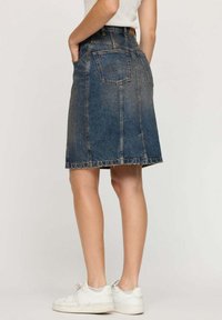 Jupe en denim bleu foncé avec une coupe droite, deux poches latérales et une poche arrière avec des détails de broderie. L'ourlet est effiloché.