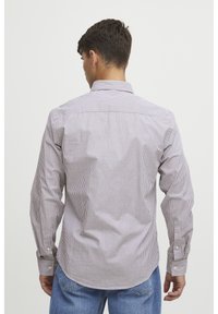 Camicia a maniche lunghe a righe in marrone chiaro e bianco, con colletto, polsini con bottone e orlo curvo. Il tessuto appare liscio e leggero.
