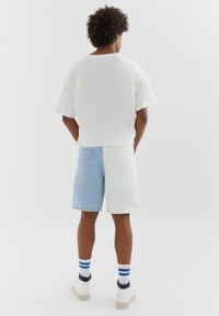 Chemise blanche oversize à manches courtes avec un col rond, associée à un short bicolore bleu clair et blanc. Baskets blanches avec des accents bleu marine.