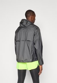 Let vægt sort jakke med hætte, der har en afslappet pasform og en bagventil detalje, parret med neongrønne shorts.