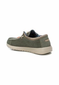 Zapatilla de lona verde tipo slip-on con acentos beige, parte superior texturizada, suela de goma y forro interior de patrón contrastante.