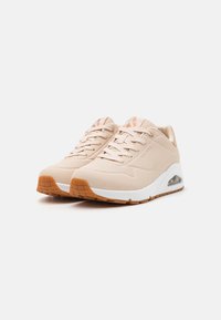 Beige sneakers med en glatt overdel, perforerte detaljer og en hvit mellomsåle. Har en gjennomsiktig luftenhet og gummisåle med teksturert grep.