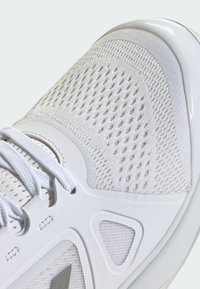 White athletic shoe with a textured upper, mesh areas for ventilation, contrasting gray accents, and a smooth rubber sole.