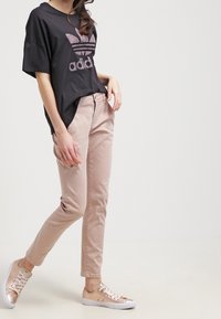 Svart oversized t-shirt med rosa logotyp, ljusrosa slim-fit byxor och metallisk rosaguld sneakers med snörning och perforerade detaljer.