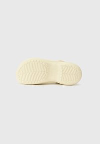 Semelle d'une chaussure beige clair avec des motifs de bande de roulement texturés pour l’adhérence, affichée sur un fond clair uni.