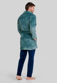 Bata de rayas turquesa con un cinturón, hecha de una tela suave; combinada con pantalones de terciopelo azul marino, que muestran un corte relajado y bolsillos.