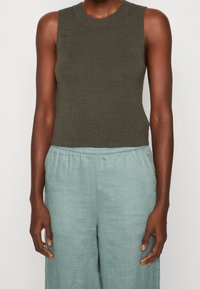 Zielono-oliwkowy, bezrękawnikowy top z prążkowanym wykończeniem w połączeniu z jasnoniebieskimi, luźnymi spodniami z lnu, posiadającymi elastyczny pas i miękką teksturę.