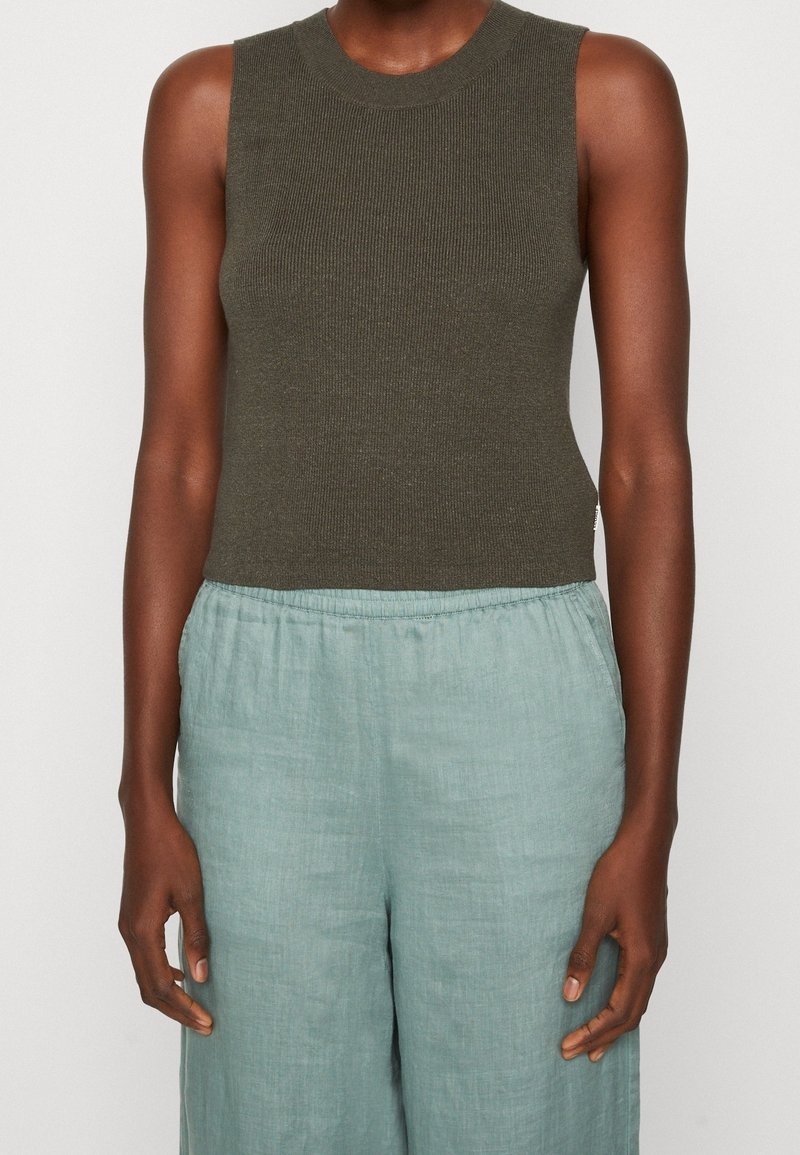 Zielono-oliwkowy, bezrękawnikowy top z prążkowanym wykończeniem w połączeniu z jasnoniebieskimi, luźnymi spodniami z lnu, posiadającymi elastyczny pas i miękką teksturę.