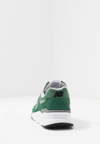 Zelené semišové a textilní tenisky s šedými akcenty, se bílou podrážkou. Design zahrnuje polstrovaný límec a logo na patě.