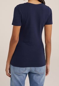 Marinblå t-shirt med kort ärm, rund halsringning, tillverkad av mjukt tyg. Skräddarsydd passform, bärs med ljusblå jeans, slät textur.