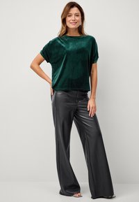 Mørkegrøn fløjel crop top med korte ærmer, parret med højtaljede sorte bukser i kunstlæder med vidde, der fremhæver en glat tekstur.