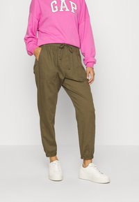 Rosa sweatshirt med "GAP" i hvid, parret med olivengrønne joggers med elastiske manchetter og snoreliv. Hvide sneakers fuldender looket.