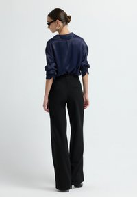 Chemise en satin bleu marine à manches retroussées, associée à un pantalon noir taille haute. Les accessoires comprennent des boucles d'oreilles créoles et des lunettes de soleil.