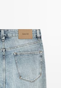 Lichtblauwe denim jeans achterkant met een enkele zak en een bruine leren patch met „Massimo Dutti“ branding.