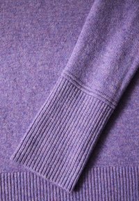 Lila gestrickter Pullover mit gerippten Bündchen, weicher Textur und dezenten Farbvariationen. Fokus auf Ärmel- und unteren Saumdetails.