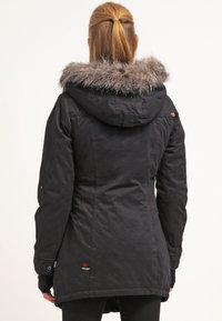 Sort hættejakke med kunstpelskant, der har en let buet søm og et logo på nedre venstre side. Glat tekstur.