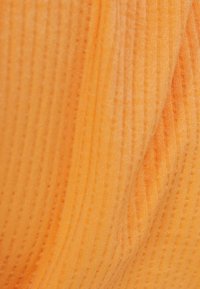 Tessuto arancione testurizzato con sottili strisce verticali, che mostra una sensazione morbida e una leggera lucentezza. Il materiale appare leggero e flessibile.