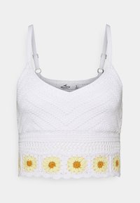 Wit gehaakt cropped top met V-hals, verstelbare bandjes en een zonnebloem borduursel langs de onderste zoom. Geharte afwerking.