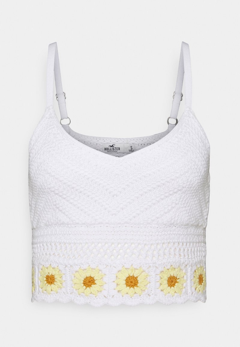 Wit gehaakt cropped top met V-hals, verstelbare bandjes en een zonnebloem borduursel langs de onderste zoom. Geharte afwerking.