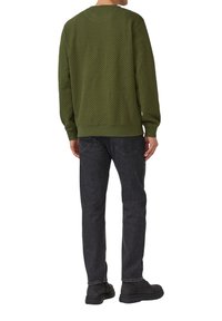 Zielona teksturowana bluza z okrągłym dekoltem, ściągaczami na rękawach i u dołu, zestawiona z ciemnoszarymi dżinsami oraz czarnym obuwiem. Widok od tyłu.