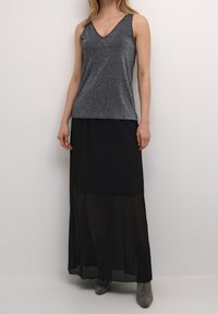 Czarna, przezroczysta długa spódnica nałożona na srebrny, teksturowany top bez rękawów z dekoltem w serek. Modelka nosi błyszczące, srebrne botki za kostkę.