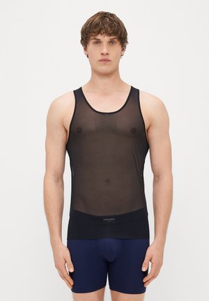 Čierne priesvitné tielko s okrúhlym výstrihom a širokými ramienkami. Má pevnú čiernu pásku na spodnej časti a je nosené na námorníckych modrých kraťasoch.