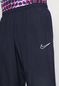 Marinblå träningsshorts med elastisk midja och vit Nike-swoosh-logga på höger lår, kombinerat med ett mönstrat linne.