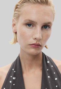 Grijze haltertop met zilveren versieringen. De stof heeft een gladde textuur en het ontwerp heeft een diepe halslijn en minimalistische styling.