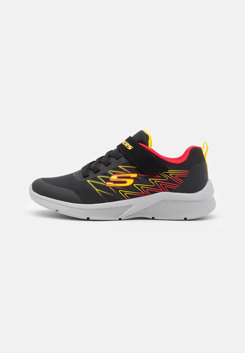 Baskets noires avec motifs en zigzag jaunes et rouges, doublure intérieure rouge, semelle grise et logo jaune sur le côté.
