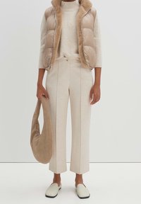 Chaleco puffer beige con cuello de piel sintética, suéter ligero, pantalones de pierna ancha crema y un suave bolso de hombro beige. Textura suave; diseño minimalista.