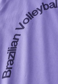 Lila Baumwoll-T-Shirt mit fettgedrucktem schwarzen Text, der geschwungen auf dem Stoff steht und "Brazilian Volleyball" liest. Glatte Textur, lässiges Design.
