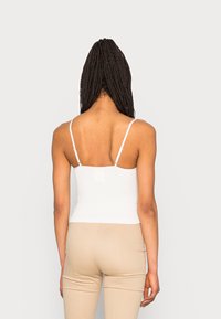 Camisola bianca a costine con spalline sottili e regolabili, design aderente e texture liscia, abbinata a pantaloni beige attillati.