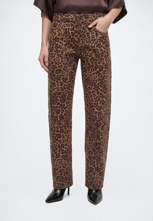 Kvinde iført brune leopardmønstrede bukser med lige ben, sorte spidse høje hæle og en mørkebrun top.